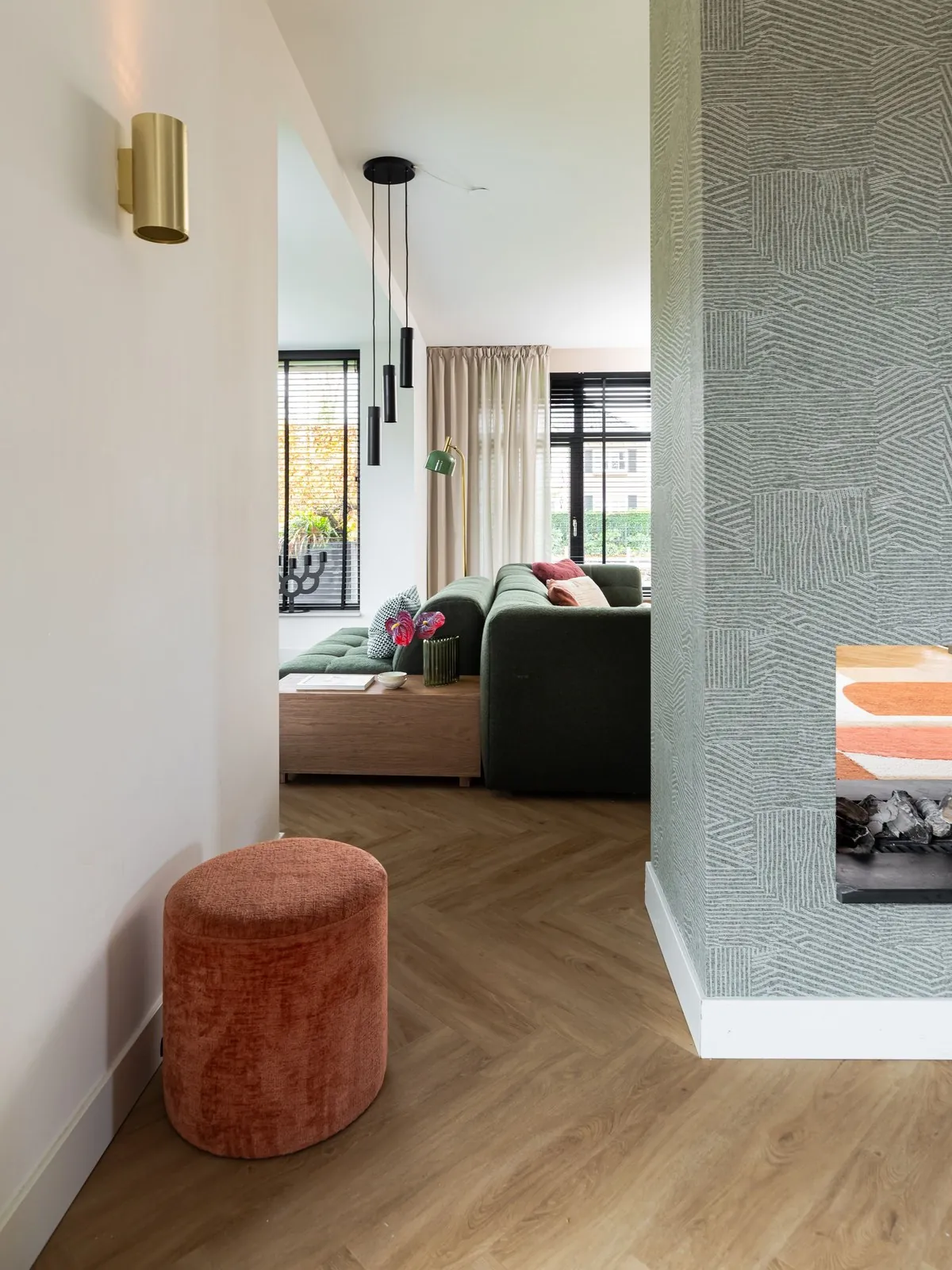 Doorkijkje naar woonkamer met erker, groene bank en haard met structuurwand in Zwolle