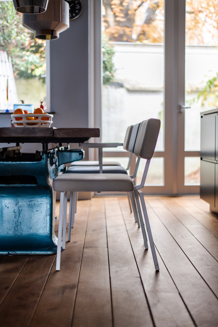 Eettafel met industriële blauwe poot en grijze stoelen, openslaande deuren naar tuin in een grachtenpand