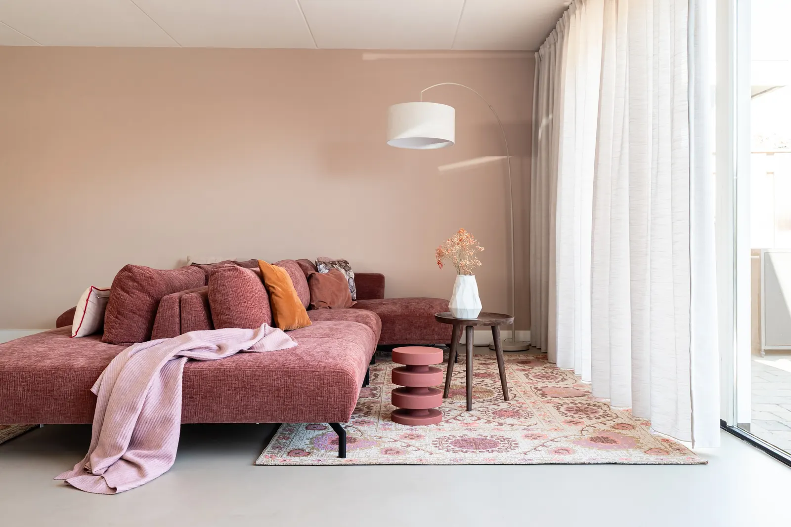 Rode hoekbank bij het raam met bloemenvloerkleed in twee-onder-een-kapwoning in Zwolle