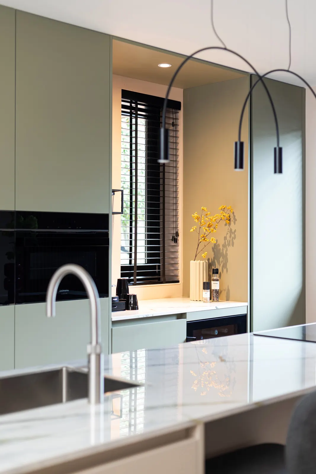 Keuken met spoelbak in het kookeiland en groene kastenwand in een villa in Zwolle